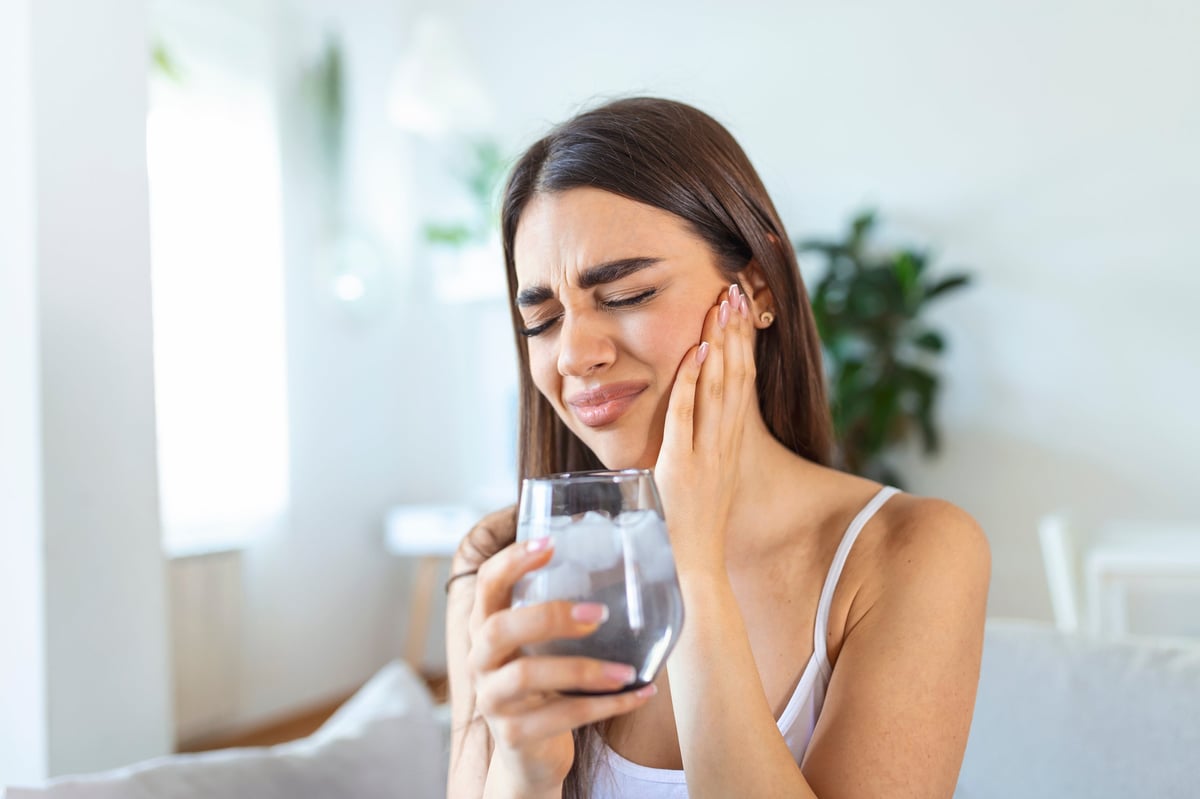 Young woman with sensitive teeth and hand holding glass of cold water with ice. Healthcare concept.