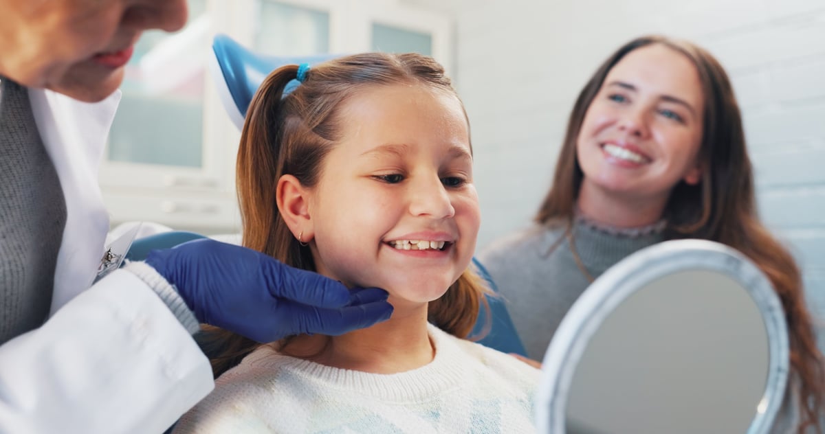 Happy child at pediatric dental clinic with parent and dentist smiling