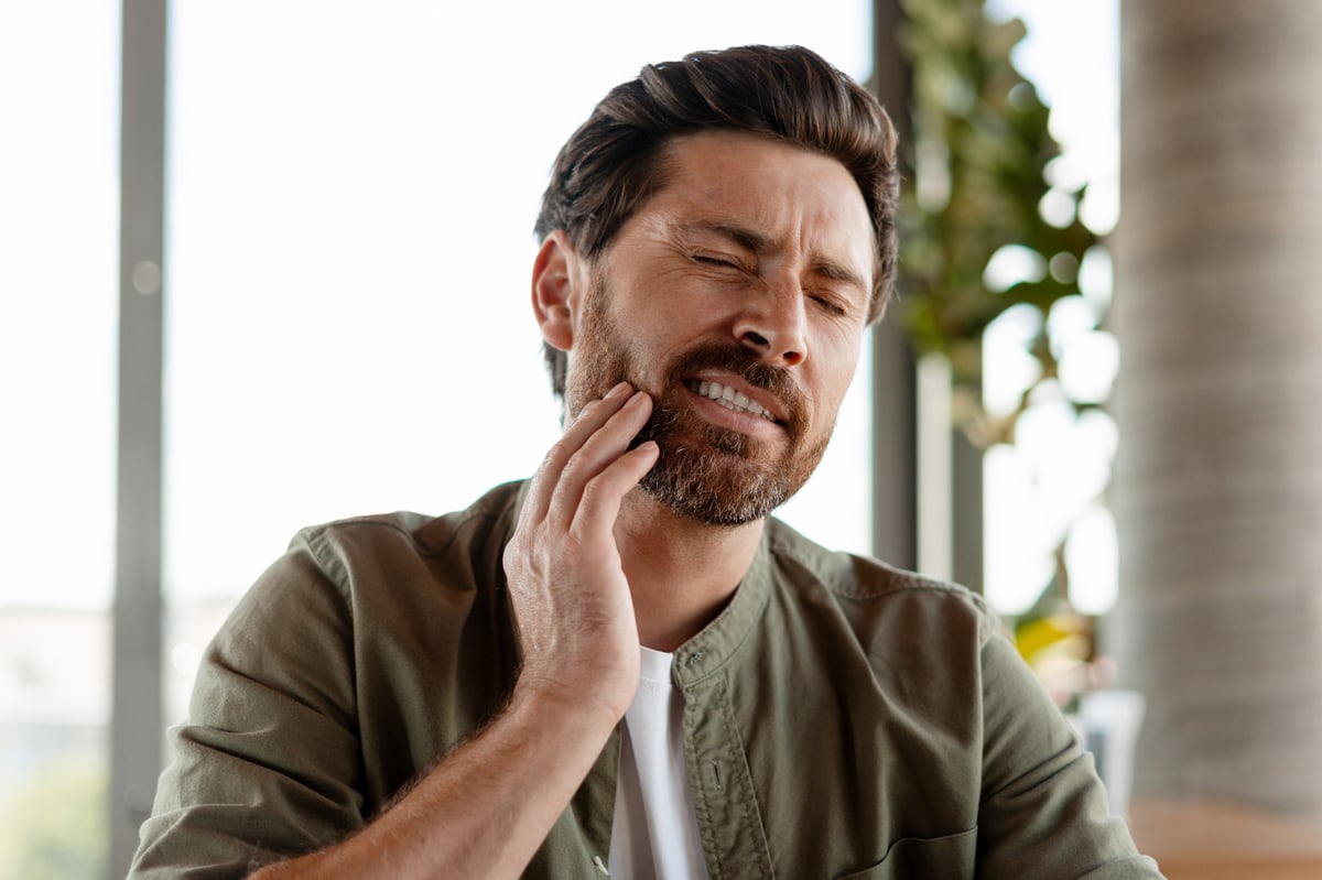 Mid adult man with a beard suffering from a strong tooth or jaw ache, touching his cheek with his hand