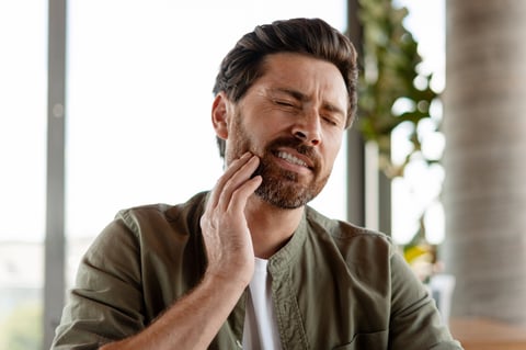 Mid adult man with a beard suffering from a strong tooth or jaw ache, touching his cheek with his hand