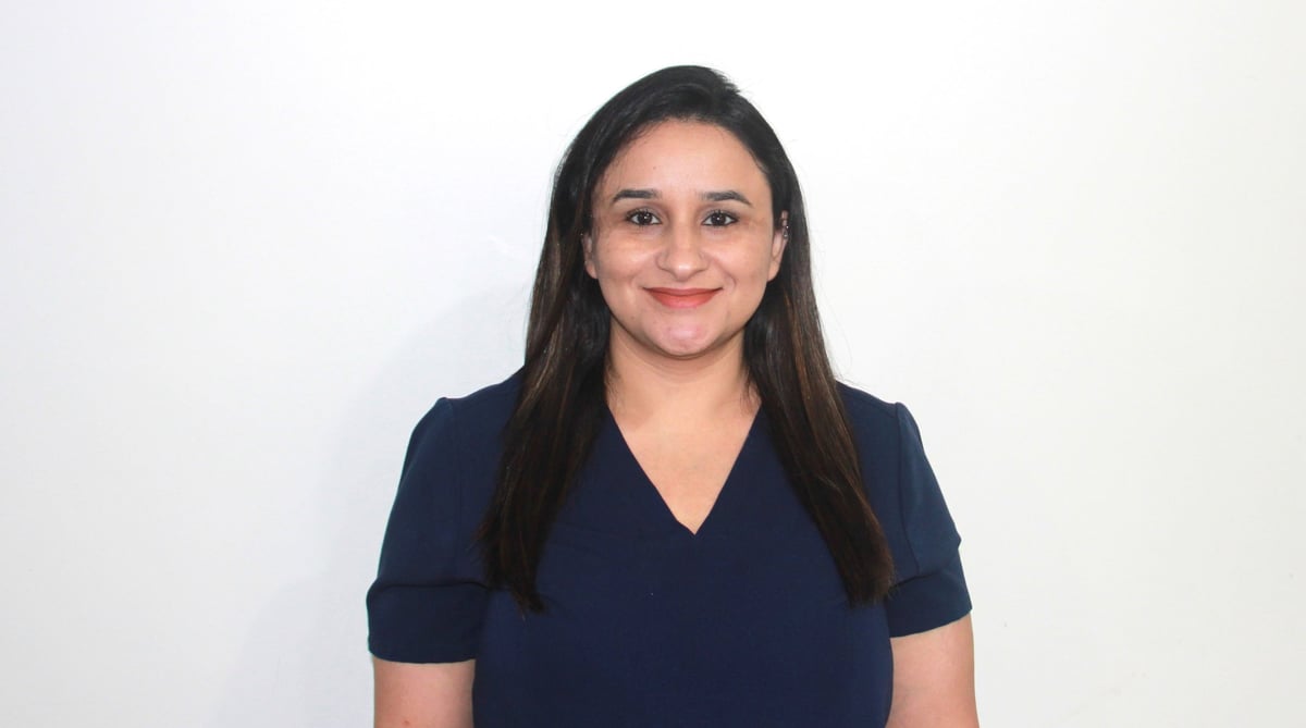 Portrait of a smiling woman with long dark hair wearing a dark blue v-neck shirt against a white background